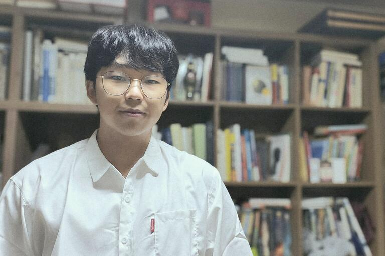 Photo of Hong Joo posing in front of library stacks
