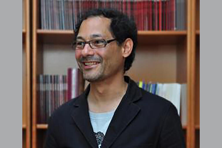smiling man with glasses gazes off camera with books in background