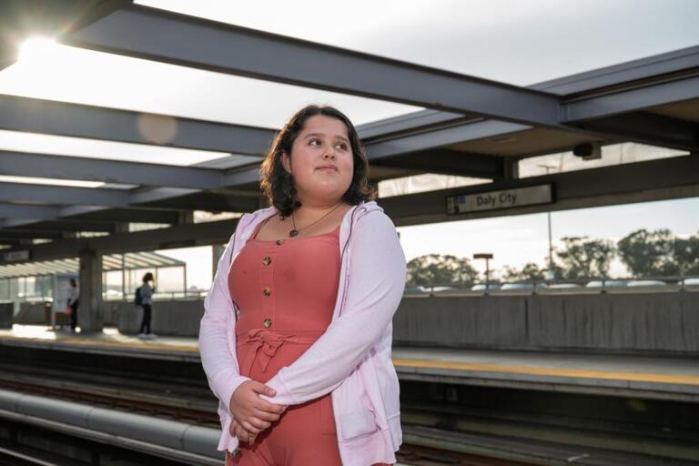 woman in peach-colored dress stands on BART platform