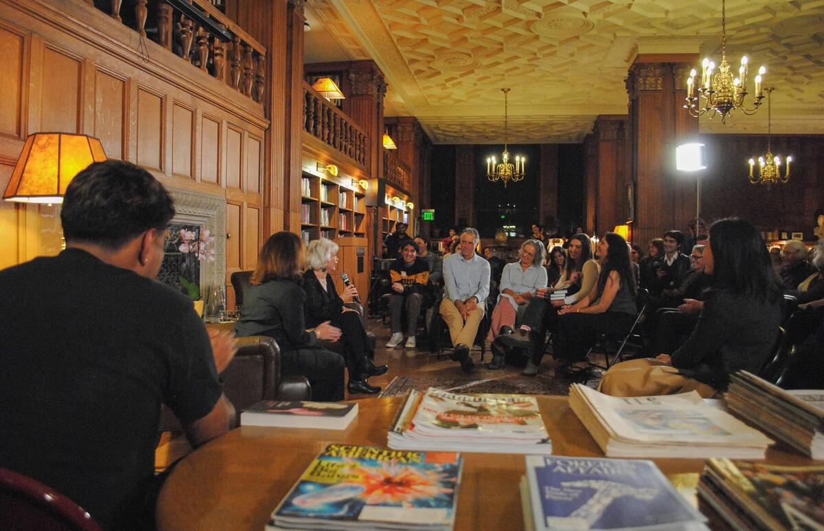 A group discussion in a warmly lit library room with chandeliers and wooden paneling.