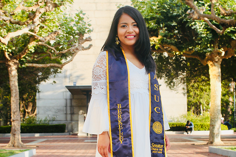 woman in white dress and graduation stole stands with campanile in background