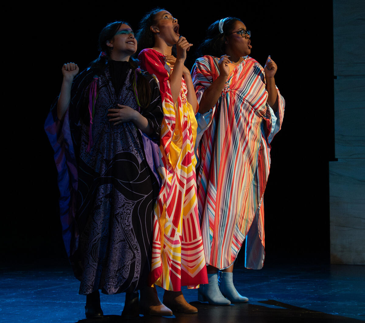three women in robes stand on stage