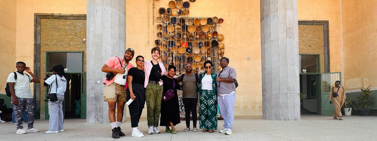 Seven people pose for a photo in front of a building with a prominent art exhibit