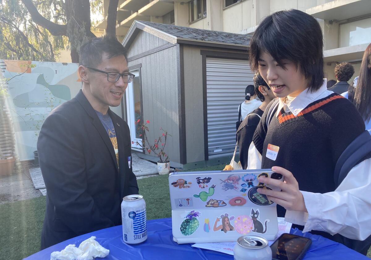 A student shows an alum their laptop screen at an outdoor reception
