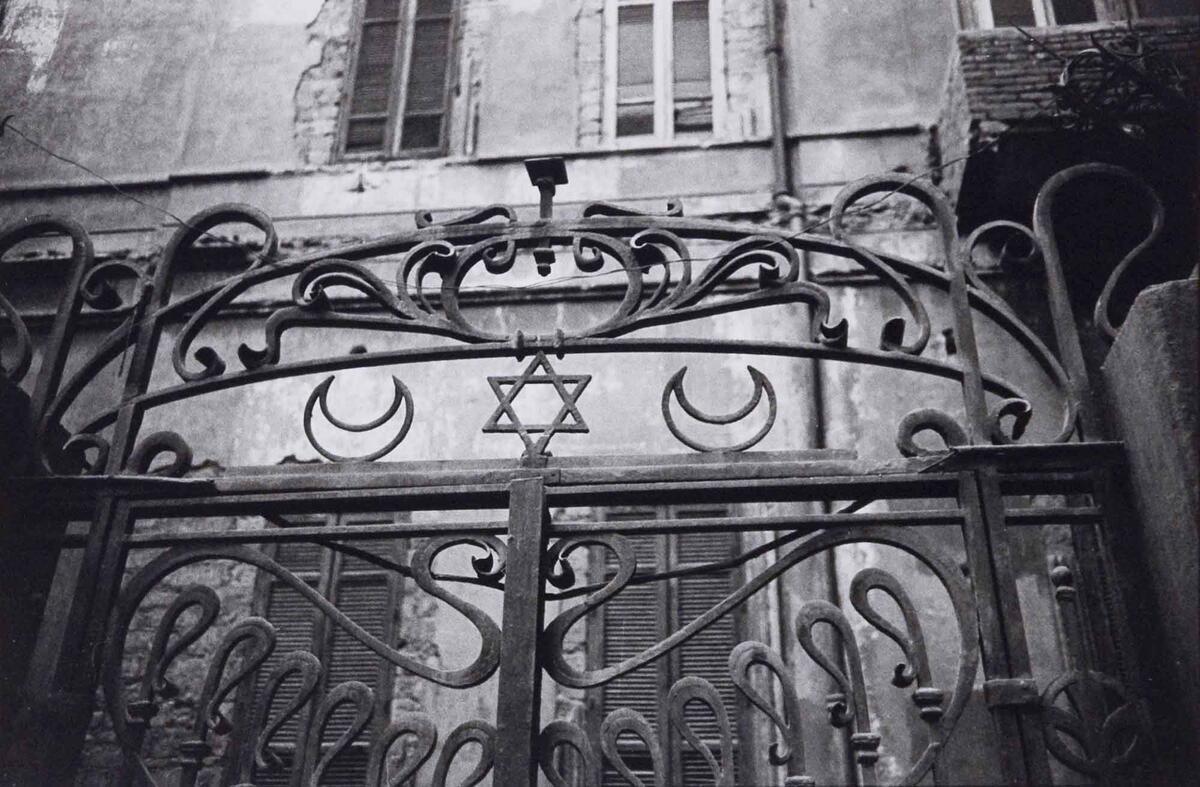 BW photo of a wrought iron gate with a Star of David flanked by two crescents