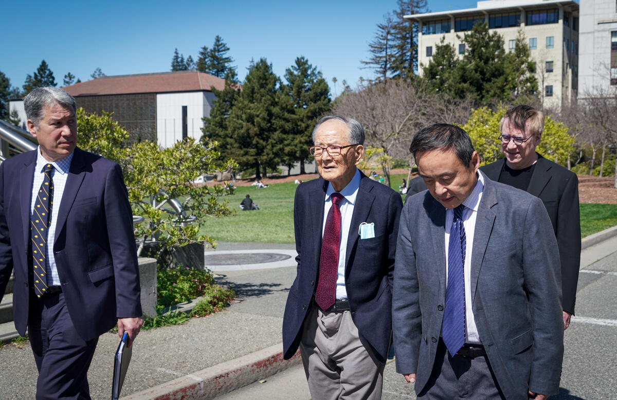 Four men in suits walk near campus libraries