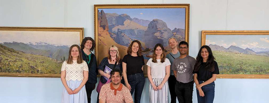 Nine people pose for a photo in front of three landscape paintings
